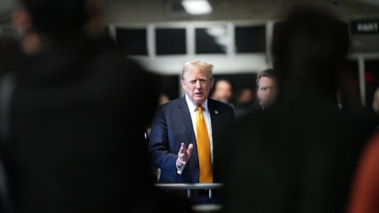 A man in a blue suit with a large orange tie speaks to reporters.