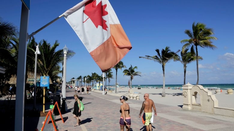 A Canadian flag flies as people walk along the boardwalk in Hollywood, Fla.