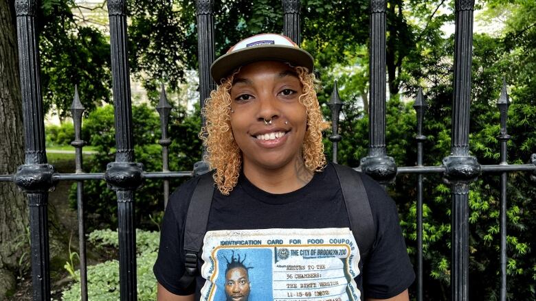 A Black woman with blonde hair smiles in front of a park gate.