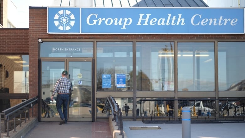 A man in a plaid shirt walks in to an office building with a sign reading Group Health Centre