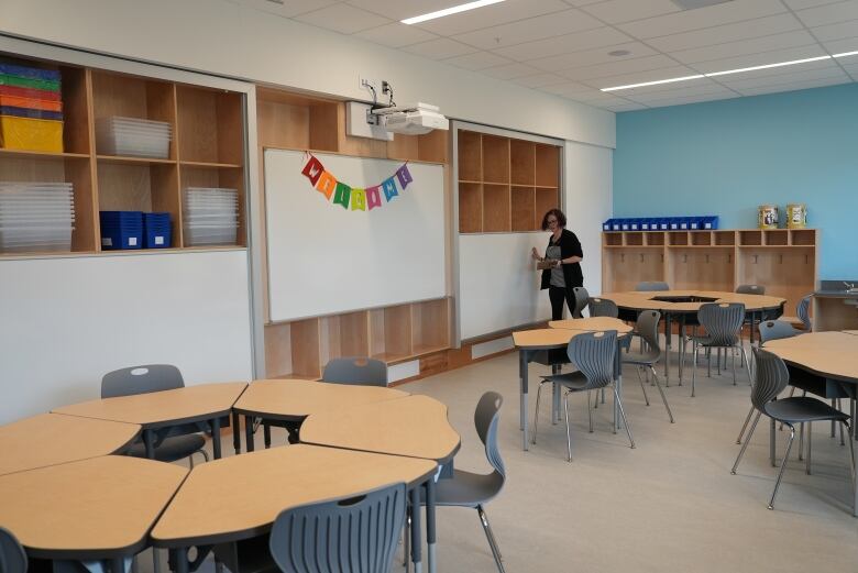 A woman stands by a whiteboard inside an empty elementary school classroom.