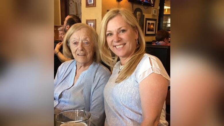 Two women smile at the camera while sitting in a booth at a restaurant.