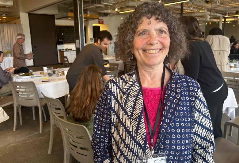 Woman with curly hair  with people sitting at tables behind her