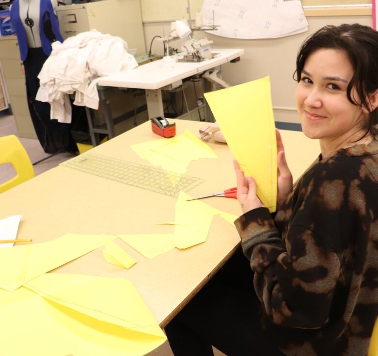 A young woman sits at a table working on a sewing project.