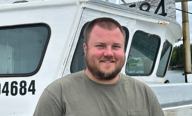 A white man with short brown hair and beard, standing in front of a boat.