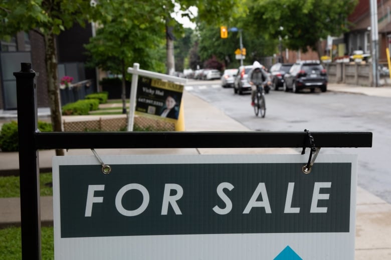 For sale signs hanf in front of houses on a street wet from rain, with a cyclist appoaching.