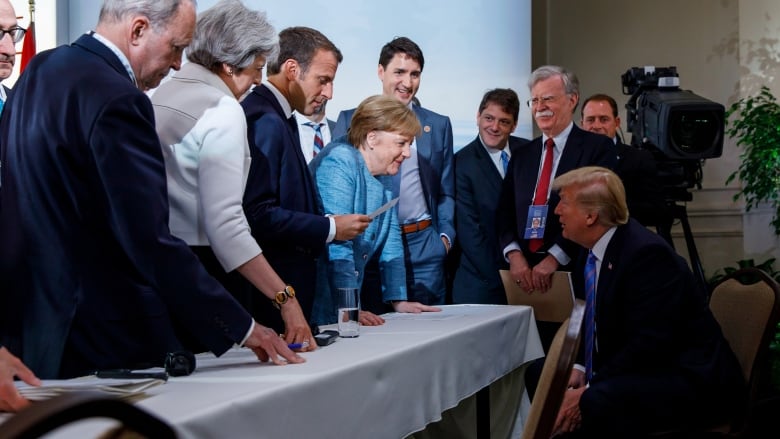 Trump seated at a desk, with other leaders crowded around him