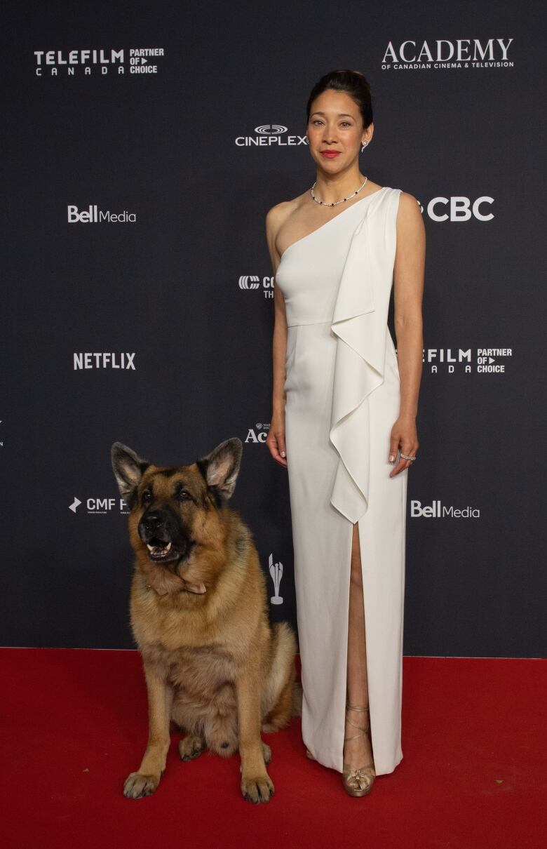 Mayko Nguyen on the Canadian Screen Awards wearing a white floor-length gown, next to Diesel vom Burgimwald the German Shepherd. 