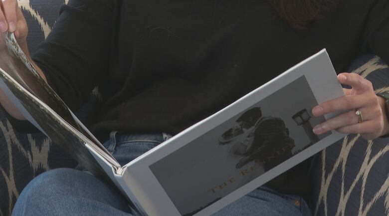 Closeup of hands holding a white hardcover book with a photo of a bride and groom embracing on the cover. 