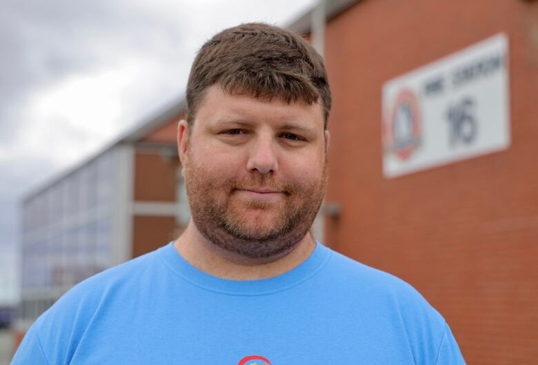 A man in a blue t-shirt stands in front of a fire hall.