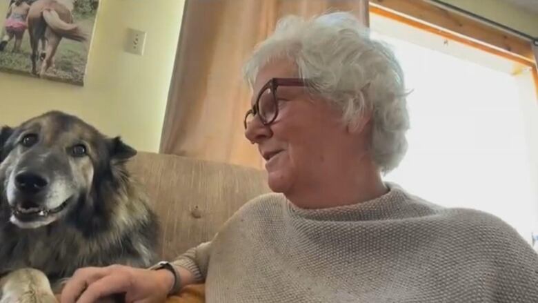 A woman with gray hair looks at a dog sitting next to her on the couch.