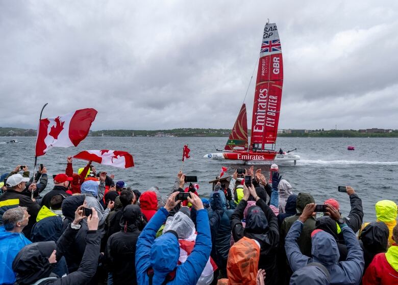 Spectators watch a SailGP boat pass by.