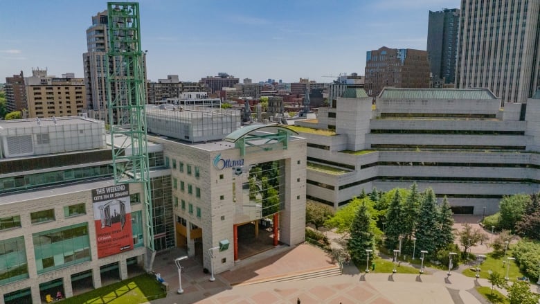 A drone view of Ottawa City Hall downtown. The sky is sunny and the trees are green. The courtyard is relatively empty.