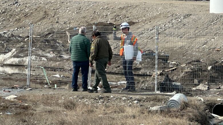 Construction workers outside a fenced off area. 