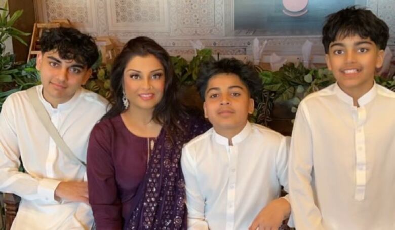 Three boys in white Indian outfits and a dark-haired woman in a purple Indian outfit sit together.