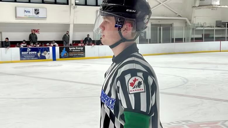 A hockey ref looks to the left of the frame while on the ice.