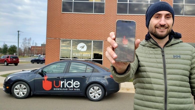 A man stands holding a cellphone up that says Uride