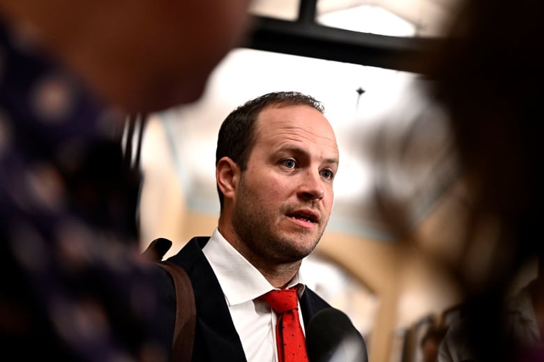 A man in a suit and red tie speaks to people not shown in the photo.