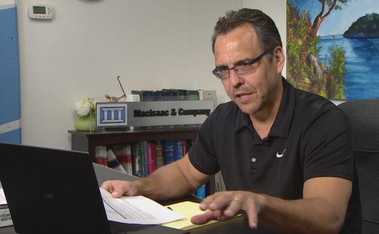 A man sits at a desk with papers and a laptop computer in an office.