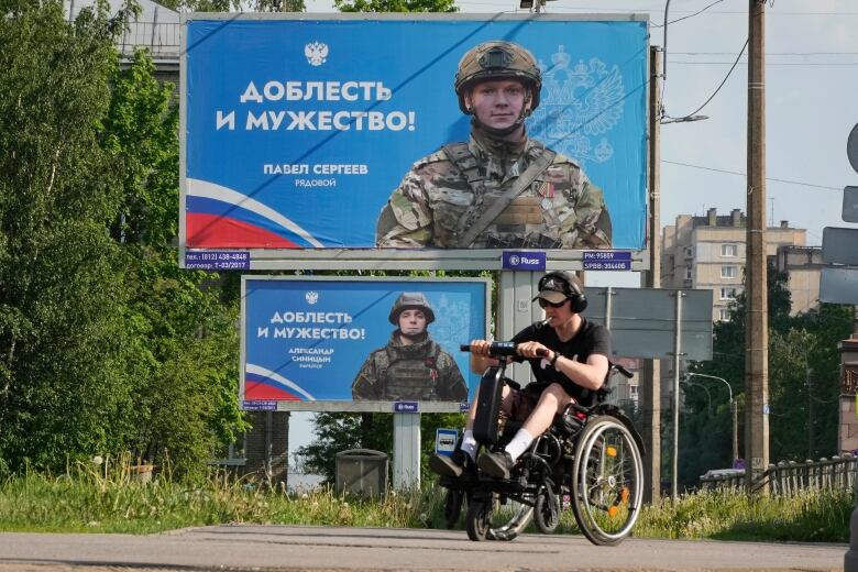 A man in a motorized wheelchair passes by a series of billboards, in St. Petersburg, Russia, showing the images of Russian soldiers involving in Russia's military campaign in Ukraine.