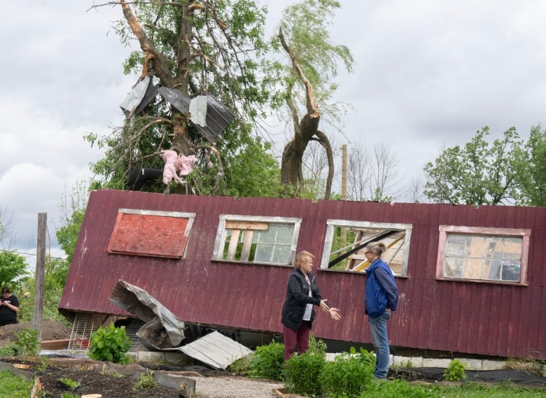 A homeowner speaks to a neighbour in front of a portion of a barn ripped apart by a tornado in Western Quebec. 