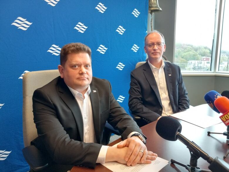 Two men in suits sitting in front of microphones.