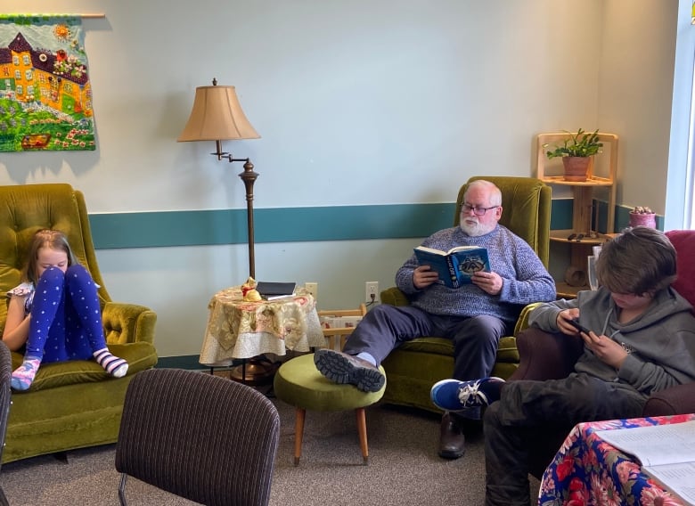 Three people curl up on soft couches and chairs with books and personal screens. 