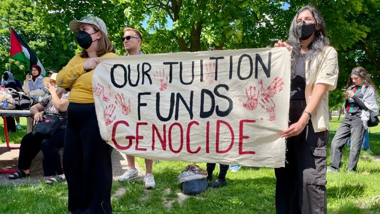 Two protesters hold up a sign at an outdoor rally.