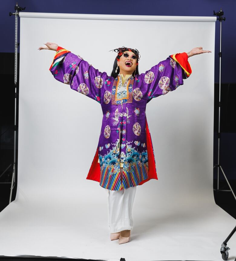 A performer in a purple dress throws their hands in the air while posing.