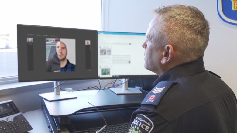 A police officer is seen sitting at a desk, looking at a computer screen