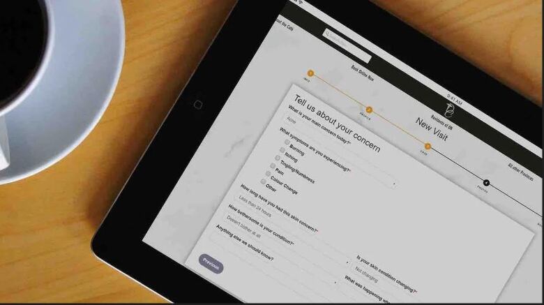 A tablet screen showing a form for an online dermatology clinic next to a cup of coffee