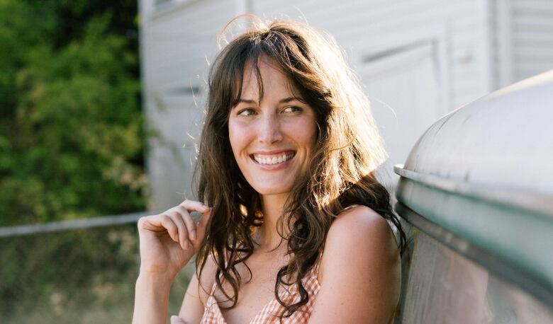 A portrait of a person in a plaid dress leaning against something metal outside. 