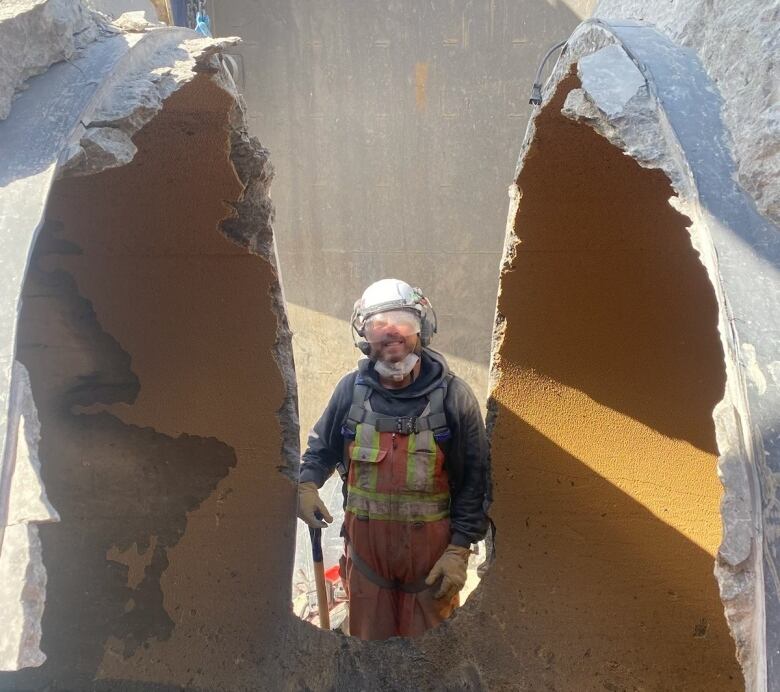 A man stands in between a half-cut concrete pipe. 