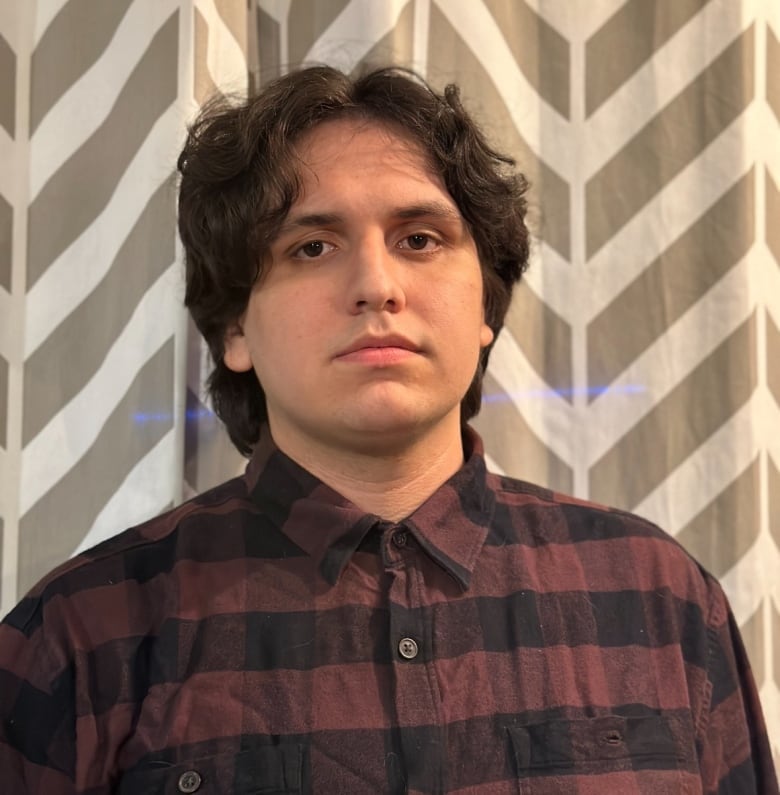 a young man with brown hair and a dark plaid button up poses for the camera