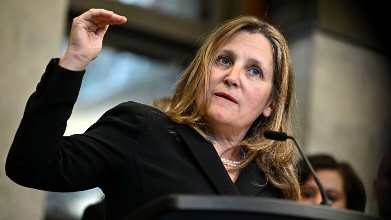 Chrystia Freeland stands at a podium holding up her hand as she discusses capital gains tax changes. 