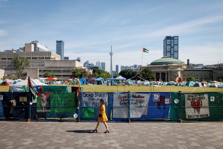 A University of Toronto graduate exits a convocation ceremony with an on-going pro-Palestinian encampment in the background at the school's downtown campus on June 4, 2024.