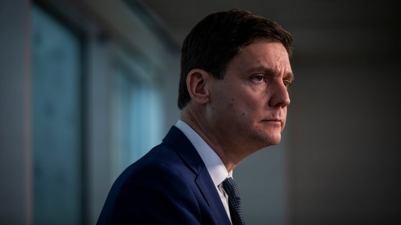 A clean-shaven man wearing a suit is pictured in profile.