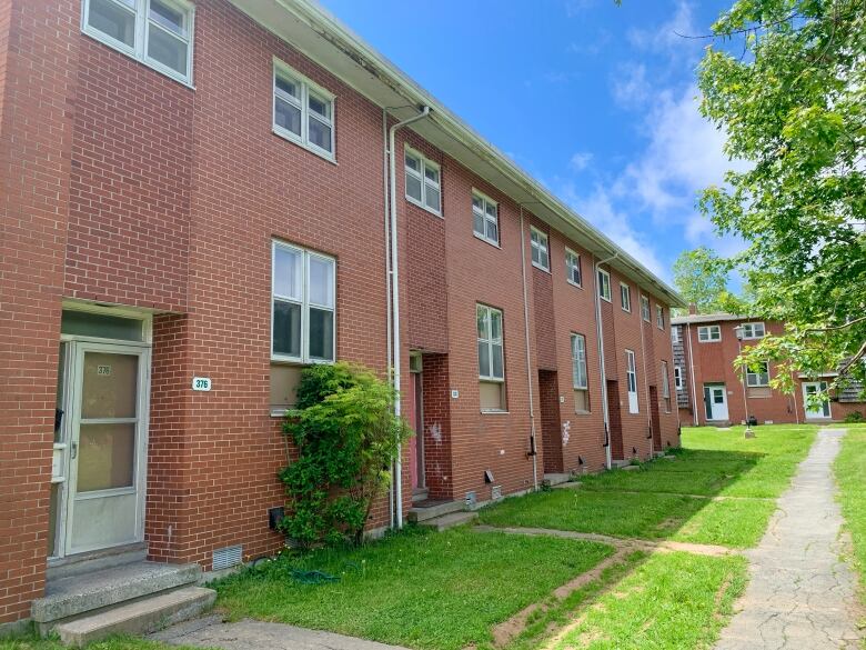 Red brick townhouses with small grass lawns an a paved pathway in front.