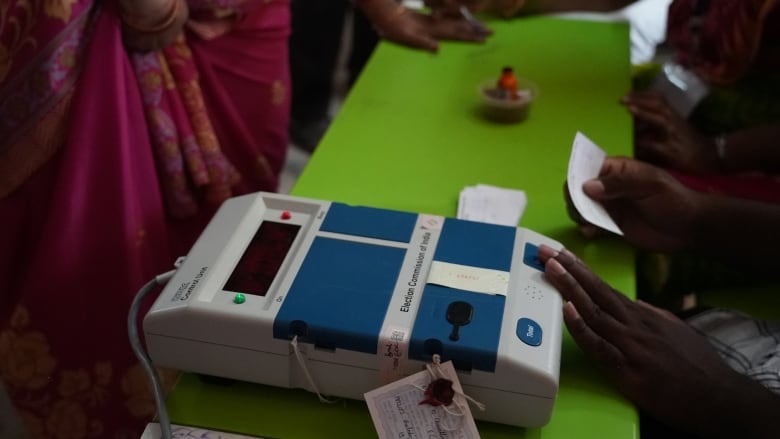 A person presses on a blue and white polling machine on top of a green table.