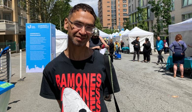 A man with glasses and black hair stands by a street festival in Vancouver. 