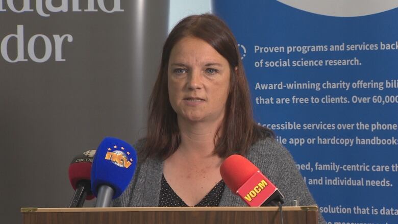 Woman with medium length brown hair speaks at a podium to reporters.