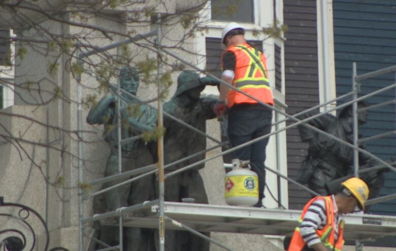 a man stands on a scaffold, with two bronze statues.