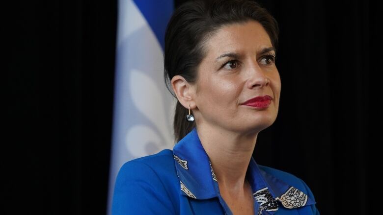 A woman sits in front of a Quebec flag, looking away from the camera