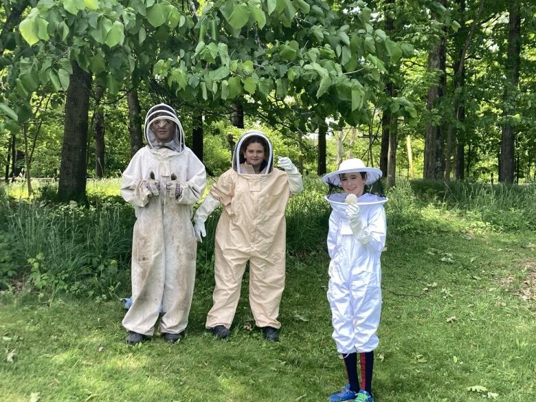 Three kids pose in beekeeping suits.