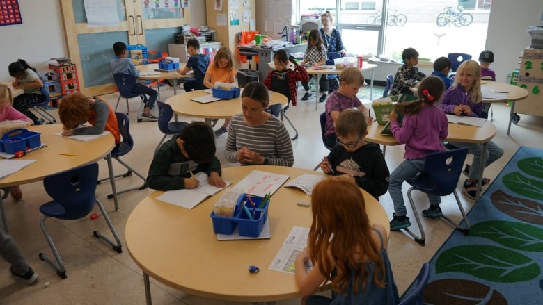 A classroom with students at shared tables working on schoolwork.