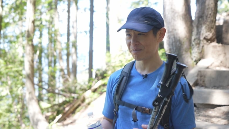 An Asian man with a blue shirt holds hiking poles. 