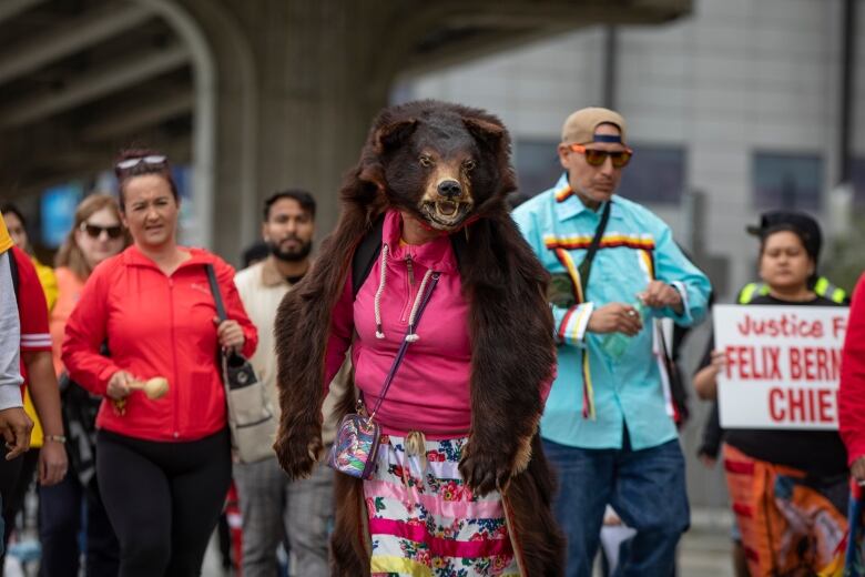 A crowd of people marching, with a woman wearing a bear suit in the middle.