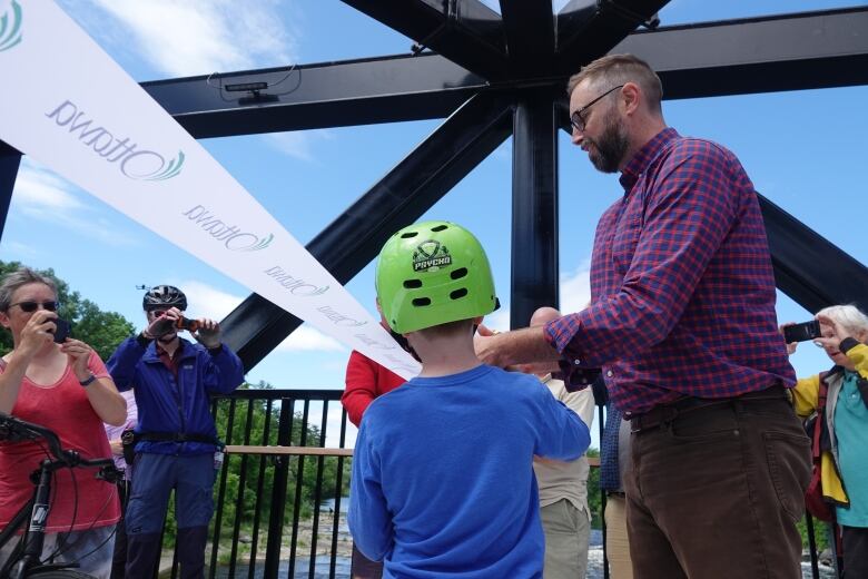 A man and a small boy in a green bike helmet cut a commemorative ribbon on a pedestrian footbridge.