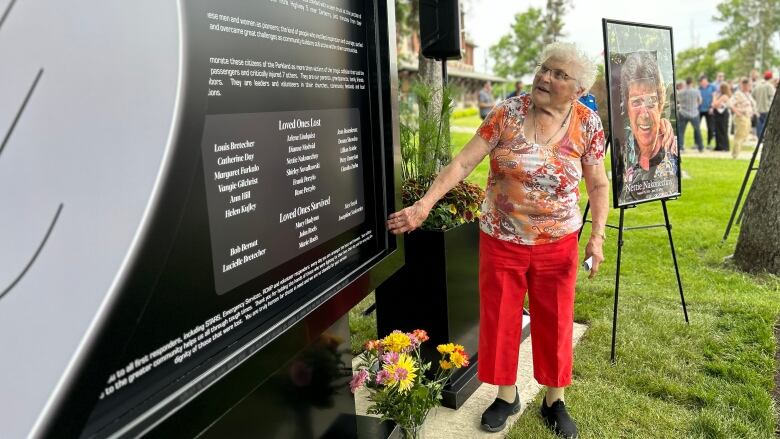 A elderly woman looks at an engraved stone monument in a park.