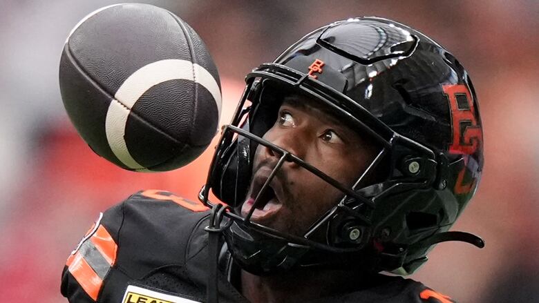 a football player in a helmet looks in shock and awe at a black football flying through the air 3 inches from his face